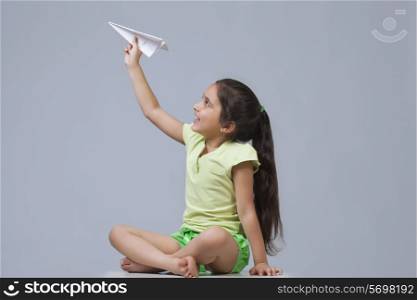Little girl playing with paper airplane isolated over blue background