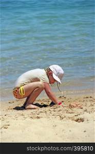 Little girl playing with sand on beach. Girl playing on sand near sea during summer holidays. Summer vacations concept. Girl playing on sand near sea during summer holidays. Summer vacations concept