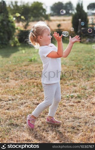 Little girl playing with soap bubbles outdoors on summer day. Real people, authentic situations