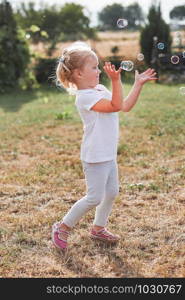 Little girl playing with soap bubbles outdoors on summer day. Real people, authentic situations