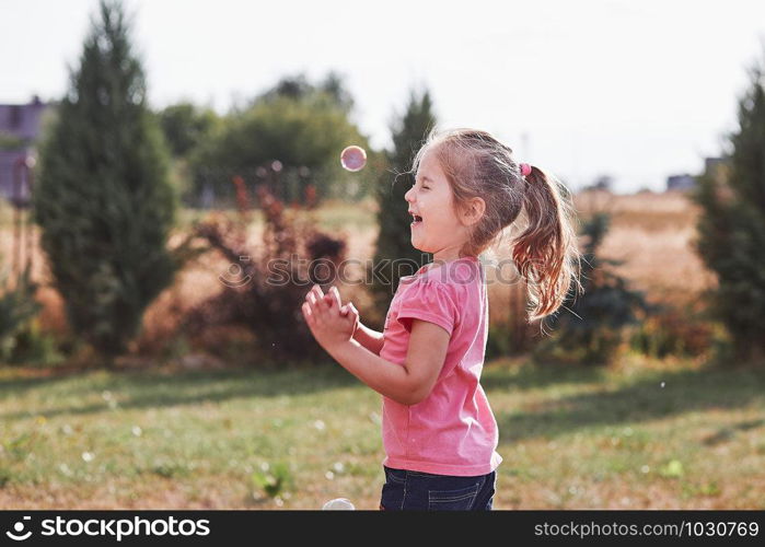 Little girl playing with soap bubbles outdoors on summer day. Real people, authentic situations