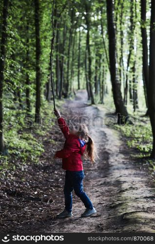 Little girl playing with stick in a forest on country road