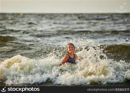 Little girl playing with waves in the sea. Kid playfully splashing with waves. Child jumping in sea waves. Summer vacation on the beach. Water splashes. Travel during summertime concept