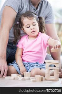 Little girl playing with wooden blocks against father in house