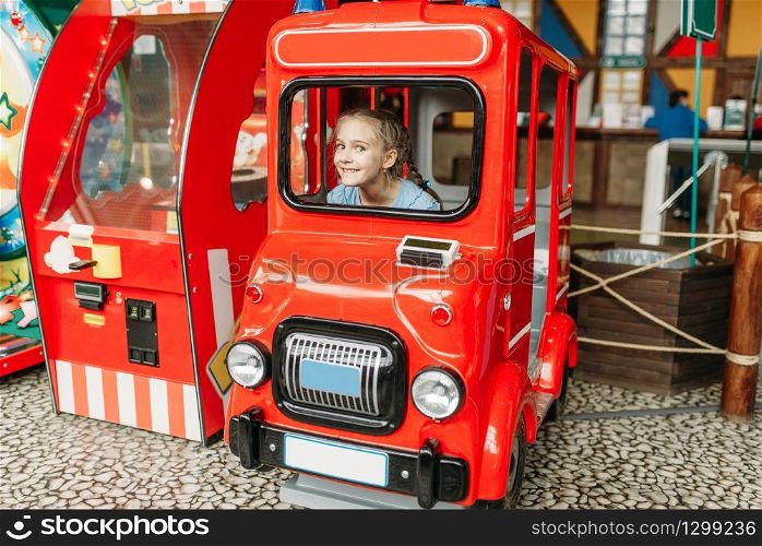 Little girl plays a bus driver, game machine, children entertainment center. Excited child having fun on playground indoors. Female kid playing in amusement centre. Little girl plays a bus driver, game machine