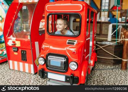 Little girl plays a bus driver, game machine, children entertainment center. Excited child having fun on playground indoors. Female kid playing in amusement centre. Little girl plays a bus driver, game machine