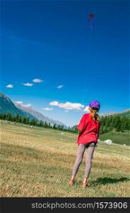 Little girl plays with her kite in large mountain meadows.