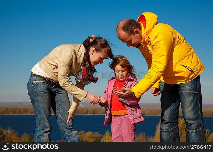 Little girl plays with parents nature in bright autumn day.