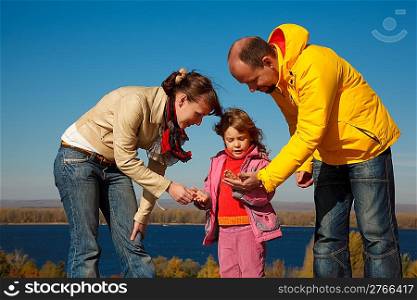 Little girl plays with parents nature in bright autumn day.