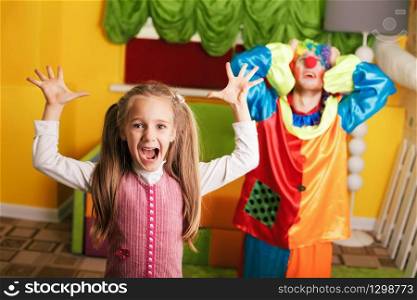 Little girl plays with upset clown at a birthday party. Colorful couch on the background.. Little girl plays with upset clown.