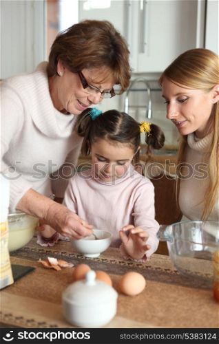 Little girl preparing cake with her mother and her grandmother