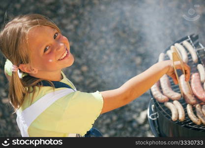 Little girl preparing meat and sausages using a barbecue grill