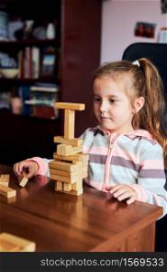 Little girl preschooler playing with wooden blocks toy building a tower. Concept of building a house