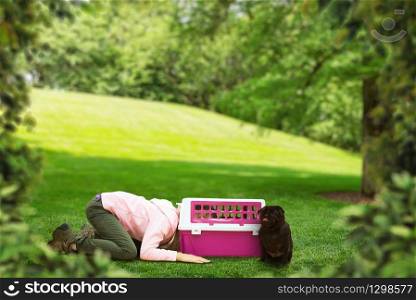 Little girl put her head into the carrier for dog on the meadow at summer day. Little girl plays with carrier for dog outdoor