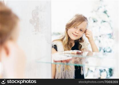 Little girl puts earrings and looking in mirror. Shallow depth of field.