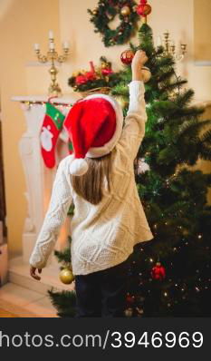 Little girl putting decorative ball on Christmas tree