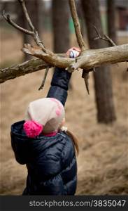 Little girl reaching for Easter egg on high tree branch