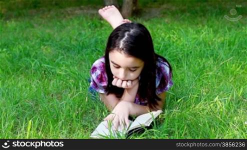 Little girl reading a book in summer park on grass