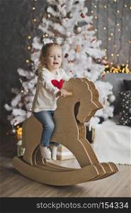Little girl riding a toy horse 7074.. Portrait of a child on paper horse in front of the tree.