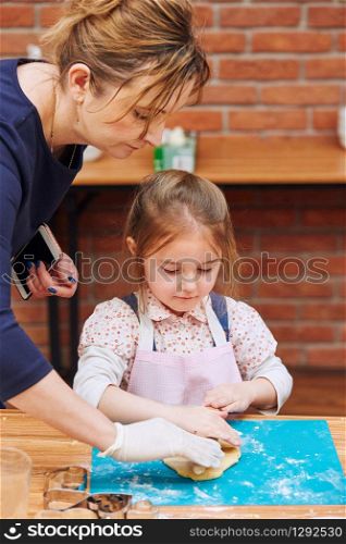 Little girl rolling the dough with her moms help for the cake. Kid taking part in baking workshop. Baking classes for children, aspiring little chefs. Learning to cook. Combining and stirring prepared ingredients. Real people, authentic situations
