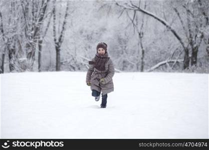 Little girl running on the background of snow covered winter park