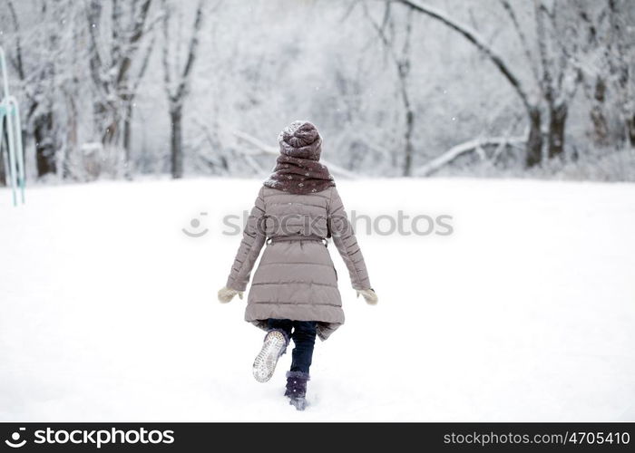 Little girl running on the background of snow covered winter park