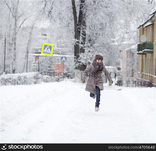 Little girl running on the background of snow covered winter park