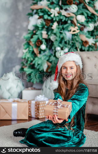 Little girl Santa Claus hat with gifts under Christmas tree sitting by the fireplace, unpacks gifts. Merry Christmas.. Little girl Santa Claus hat with gifts under Christmas tree sitting by the fireplace, unpacks gifts.