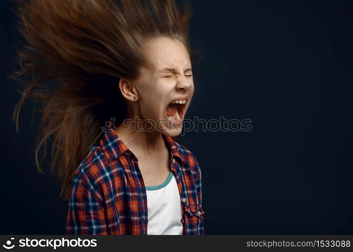 Little girl screams in studio, developing hair effect. Children and wind, kid isolated on dark background, child emotion. Little girl screams in studio, developing hair