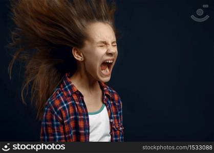 Little girl screams in studio, developing hair effect. Children and wind, kid isolated on dark background, child emotion. Little girl screams in studio, developing hair