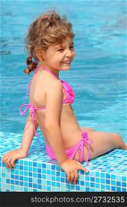 little girl sits on border of pool