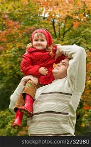 little girl sits on shoulder at man In park in autumn