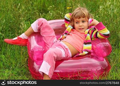 little girl sits talks by toy phone in inflatable armchair on lawn
