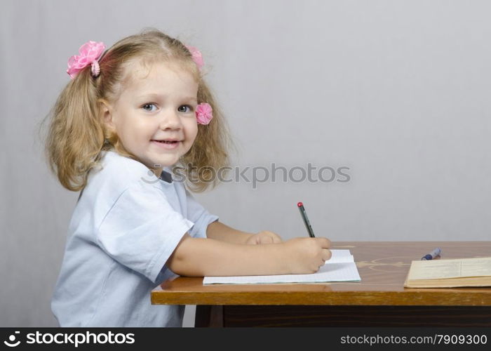 Little girl sitting at the table and writes handle in a notebook. The girl was distracted and looked to the right.