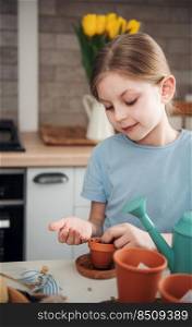 Little girl sitting at the table at home, sowing seeds into flower pots. Home gardening 