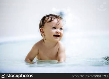 Little girl sitting in a shallow pool, laughing. Toddler. Playing in the water.. Laughing girl sitting in a shallow pool