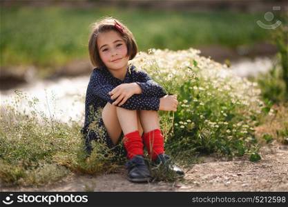 Little girl sitting in nature field wearing beautiful dress with flowers in her hand.