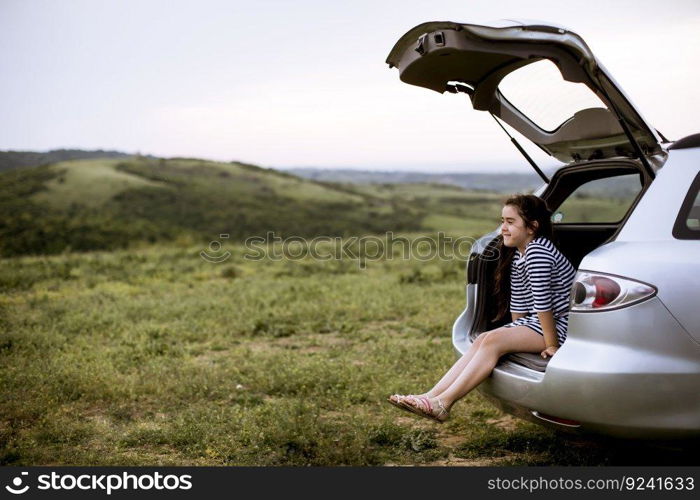 Little girl sitting in open trunk of car and looking at nature