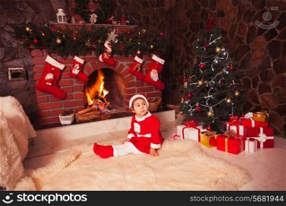 Little girl sitting near fireplace and christmas tree with gift boxes