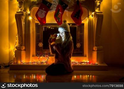 Little girl sitting next to extinguished fireplace and looking at Christmas gifts