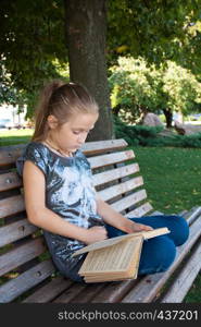 little girl sitting on a bench at the park and reading.