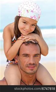 little girl sitting on father&acute;s shoulders on the beach