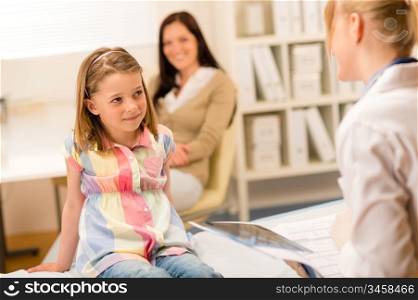Little girl sitting on medical bed listening to pediatrician
