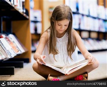 Little girl sitting on the floor and reading books in library. I love reading