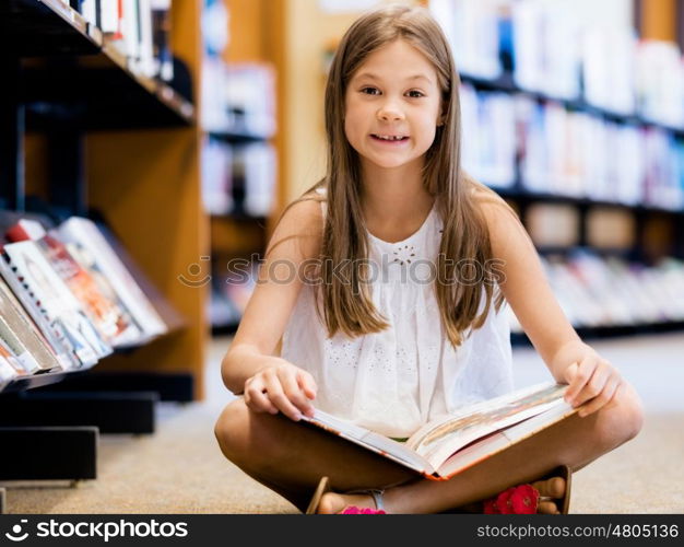 Little girl sitting on the floor and reading books in library. I love reading