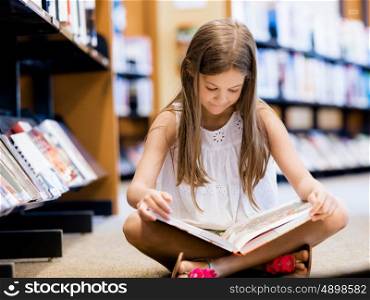 Little girl sitting on the floor and reading books in library. I love reading