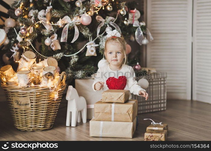 Little girl sitting under the Christmas tree with gifts.. Portrait of a child sitting on the floor near the Christmas tree 7246.