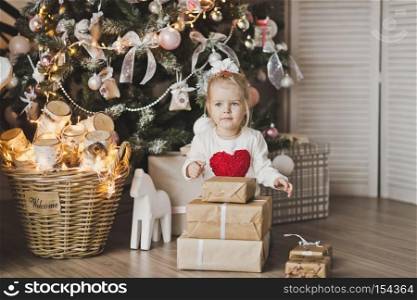 Little girl sitting under the Christmas tree with gifts.. Portrait of a child sitting on the floor near the Christmas tree 7246.