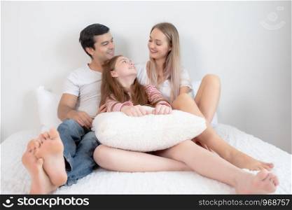 little girl smiling with mother and father on bed together in bedroom at home, young happy family concept