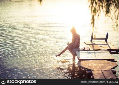 little girl splashing at the lake sitting on a wooden pier at the sunset time